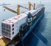 Containerschiff mit einer großen Chemieanlage im Hafen