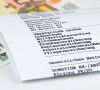 Zusammengefaltete Papier-Gehaltsabrechnung liegt auf einem 50- und einem 100-Euro-Schein